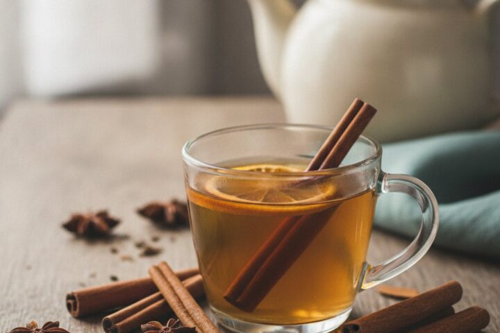 Chá de canela servido em xícara de vidro com paus de canela ao lado